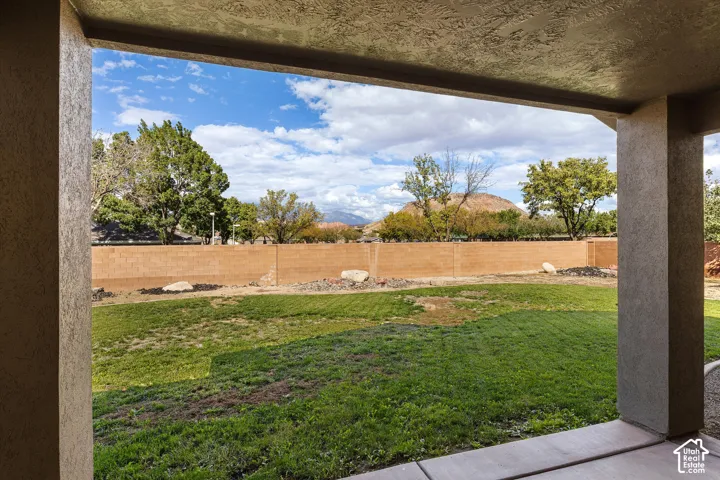 Covered concrete patio overlooking a backyard with a lawn, rock landscaping, masonry perimeter wall, and mountain backdrop