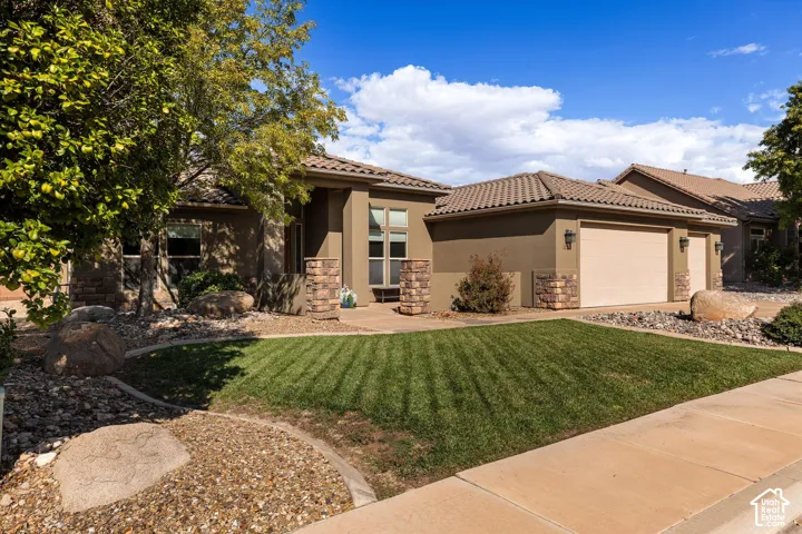 Stucco exterior with stone veneer accents, multi-car garage, concrete tile roof, and landscaped front yard with decorative boulders