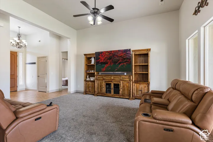 High-ceiling living area featuring neutral wall tones, carpeted flooring, a ceiling fan with integrated lighting, and built-in wood cabinetry