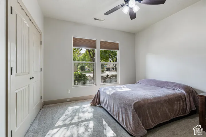 Neutral-toned interior featuring dual-pane windows with integrated blinds, wall-to-wall carpeting, a ceiling fan with integrated lighting, and a double-door closet
