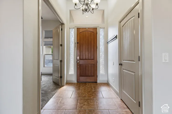 Entryway featuring stone-finish tile flooring, a solid wood arched-top entry door, sidelights with textured glass, an overhead chandelier, and interior three-panel doors