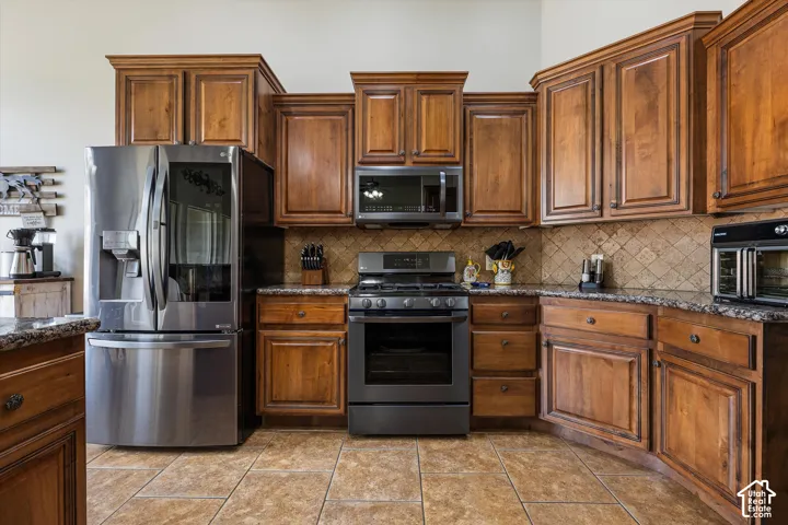 Kitchen featuring custom wood cabinetry, dark stone countertops, stainless steel appliances, and a diagonal tile backsplash