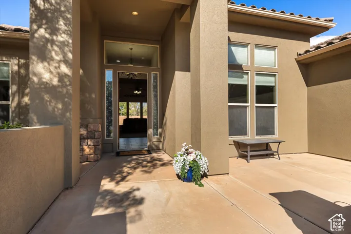 Stucco facade entrance featuring a covered patio, tile roof, masonry stone detailing, and multi-pane transom windows