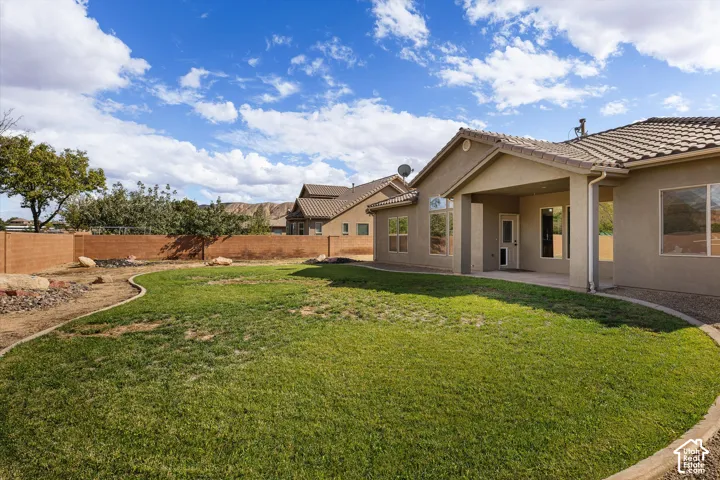 Rear exterior featuring a covered patio, grass lawn, stone landscaping accents, and perimeter masonry wall