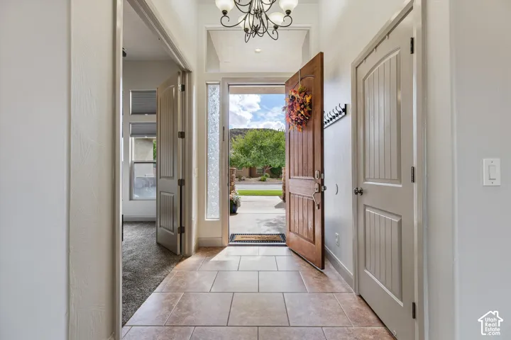 Entryway featuring tile flooring, a wood-grain paneled front door, a decorative multi-bulb chandelier, a textured glass sidelight, and arched-top interior doors