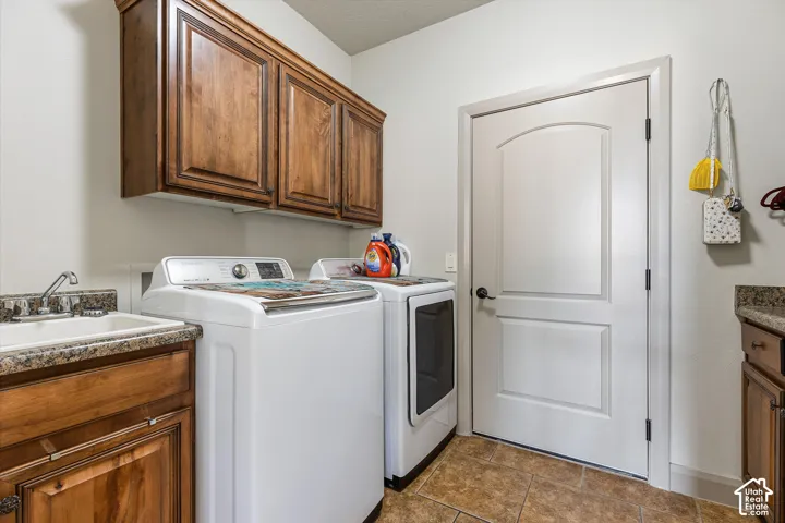 Utility area featuring wood-finish cabinetry, stone-texture countertops, tile flooring, and a drop-in sink with a chrome faucet