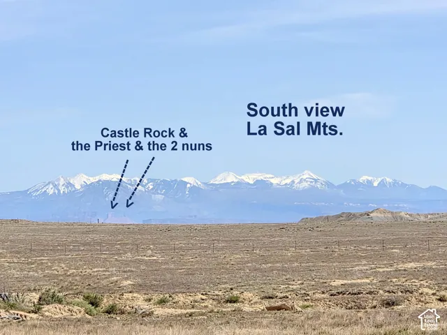 Expansive landscape featuring snow-capped peaks of the La Sal Mountains, Castle Rock, and prominent rock formations including The Priest and The Nuns