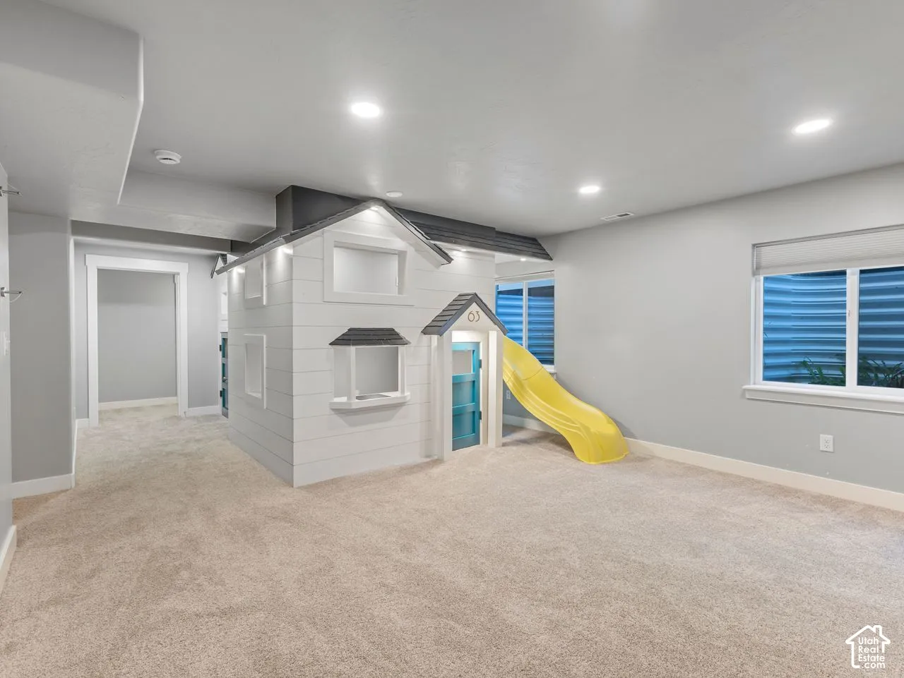Interior space featuring neutral-toned carpeting, recessed lighting, white horizontal-plank built-in play structure with a slide, and recessed window with egress well