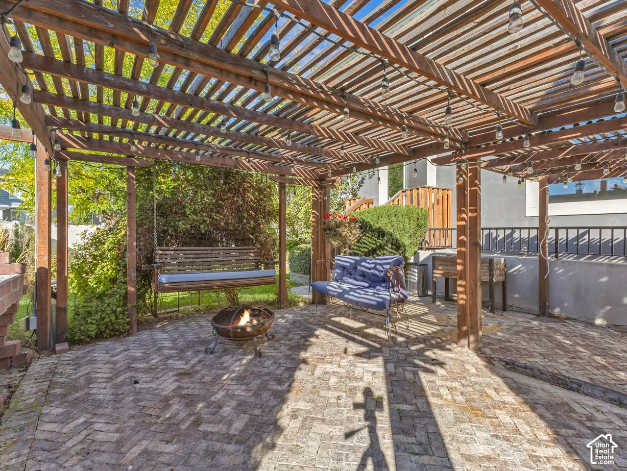 Outdoor living space featuring a wood-beam pergola with integrated string lighting and herringbone-patterned brick paver flooring
