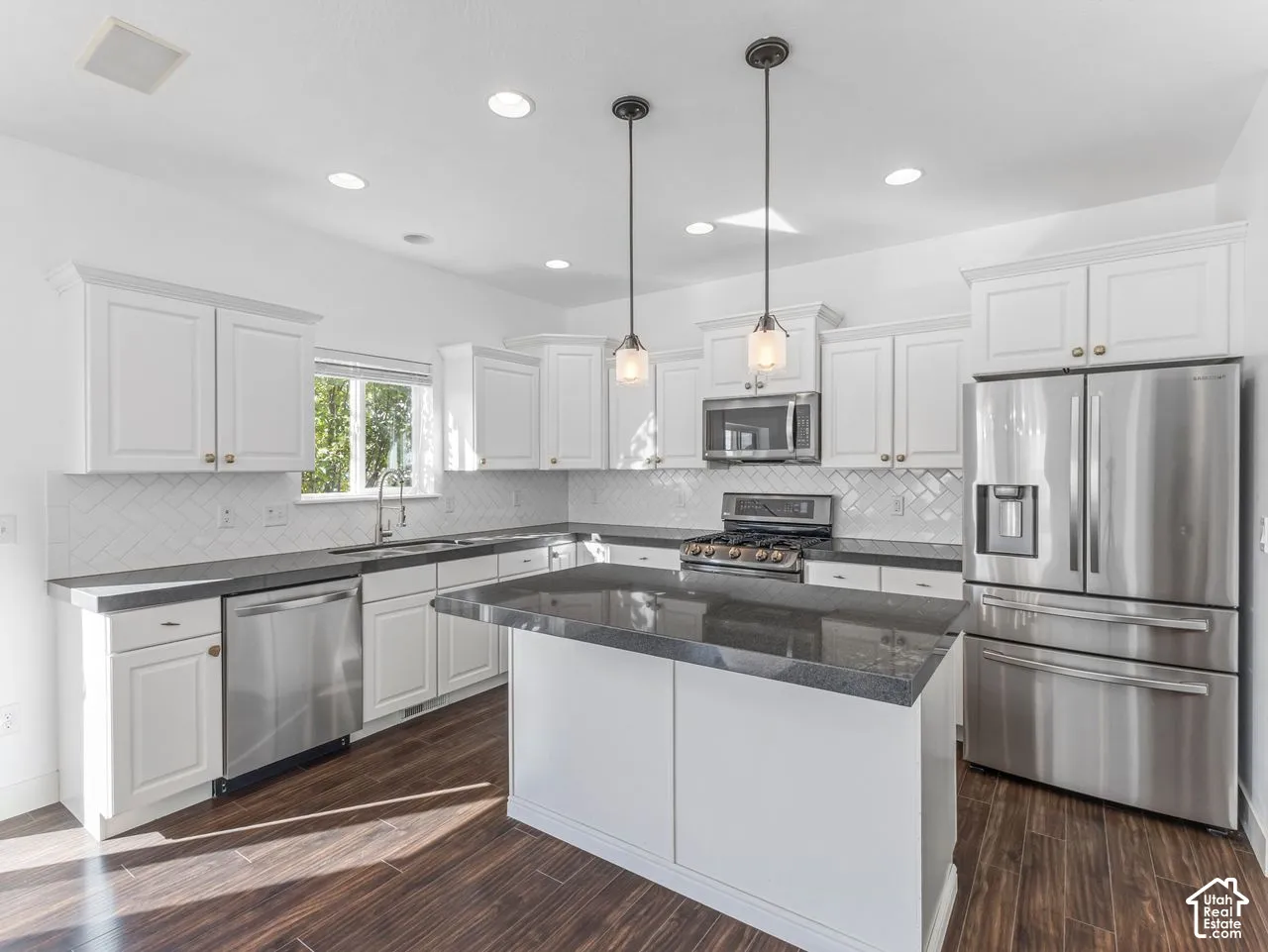 Kitchen featuring white shaker-style cabinetry, dark stone countertops, stainless steel appliances, a herringbone-pattern tile backsplash, and wood-finish flooring