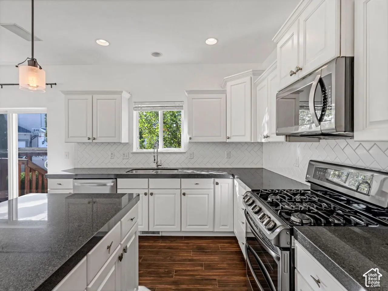 Kitchen featuring white shaker-style cabinetry, stone countertops, a herringbone tile backsplash, stainless steel appliances, and wood-finish flooring