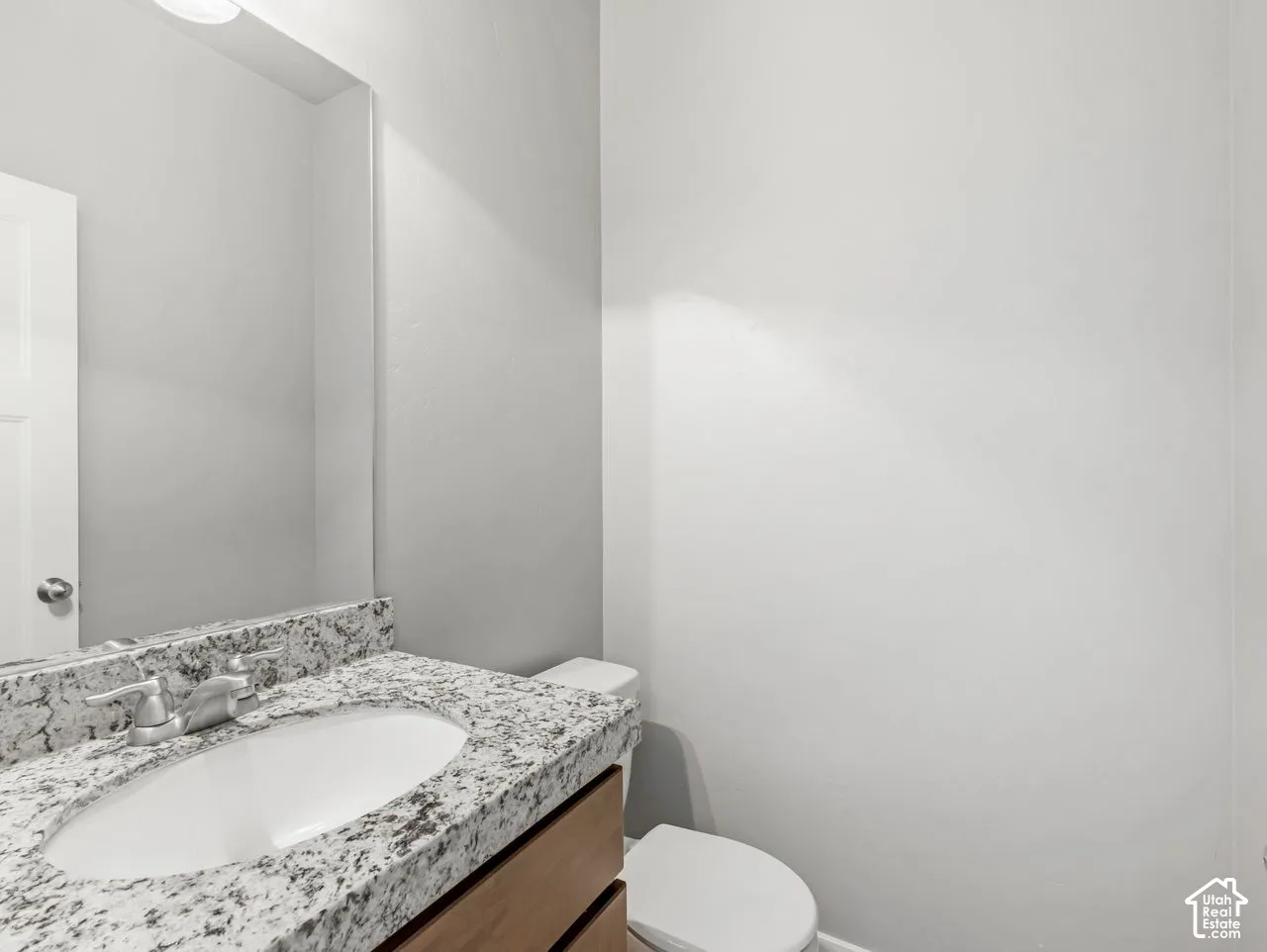 Vanity featuring a stone countertop, oval undermount sink, chrome faucet, wood-finish cabinetry, and a large wall-mounted mirror