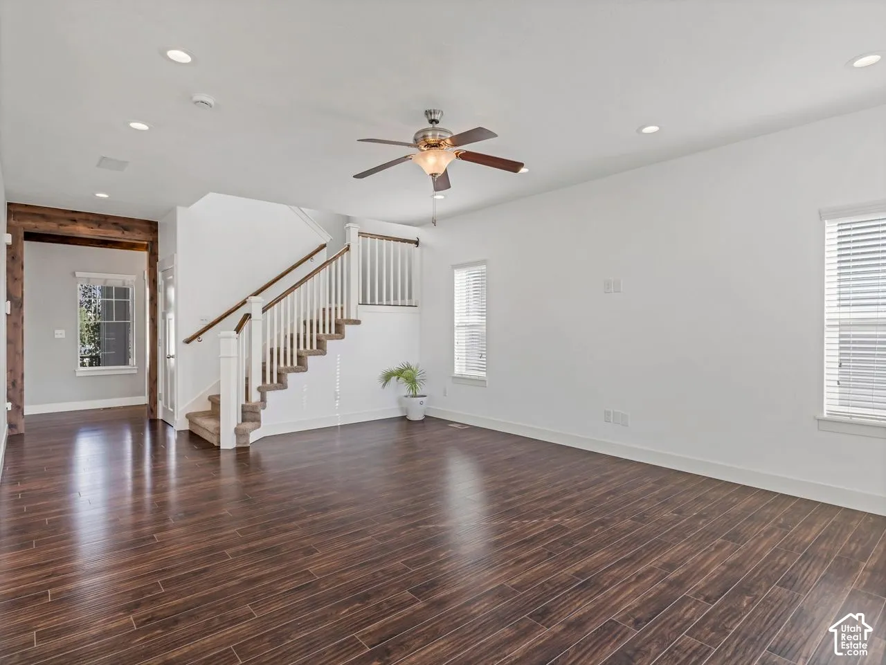 Open-concept interior featuring dark wood-finish flooring, recessed lighting, a ceiling fan with integrated light fixture, and a staircase with white balusters and a dark wood handrail