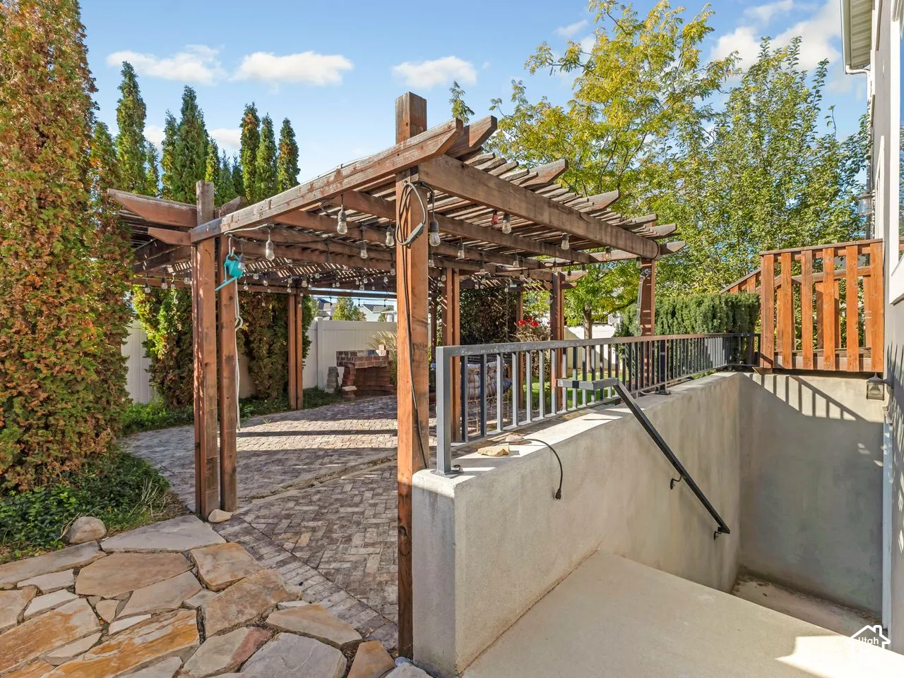 Outdoor living area featuring a wood pergola, herringbone-pattern brick patio, concrete stairway with metal railing, and natural stone hardscaping