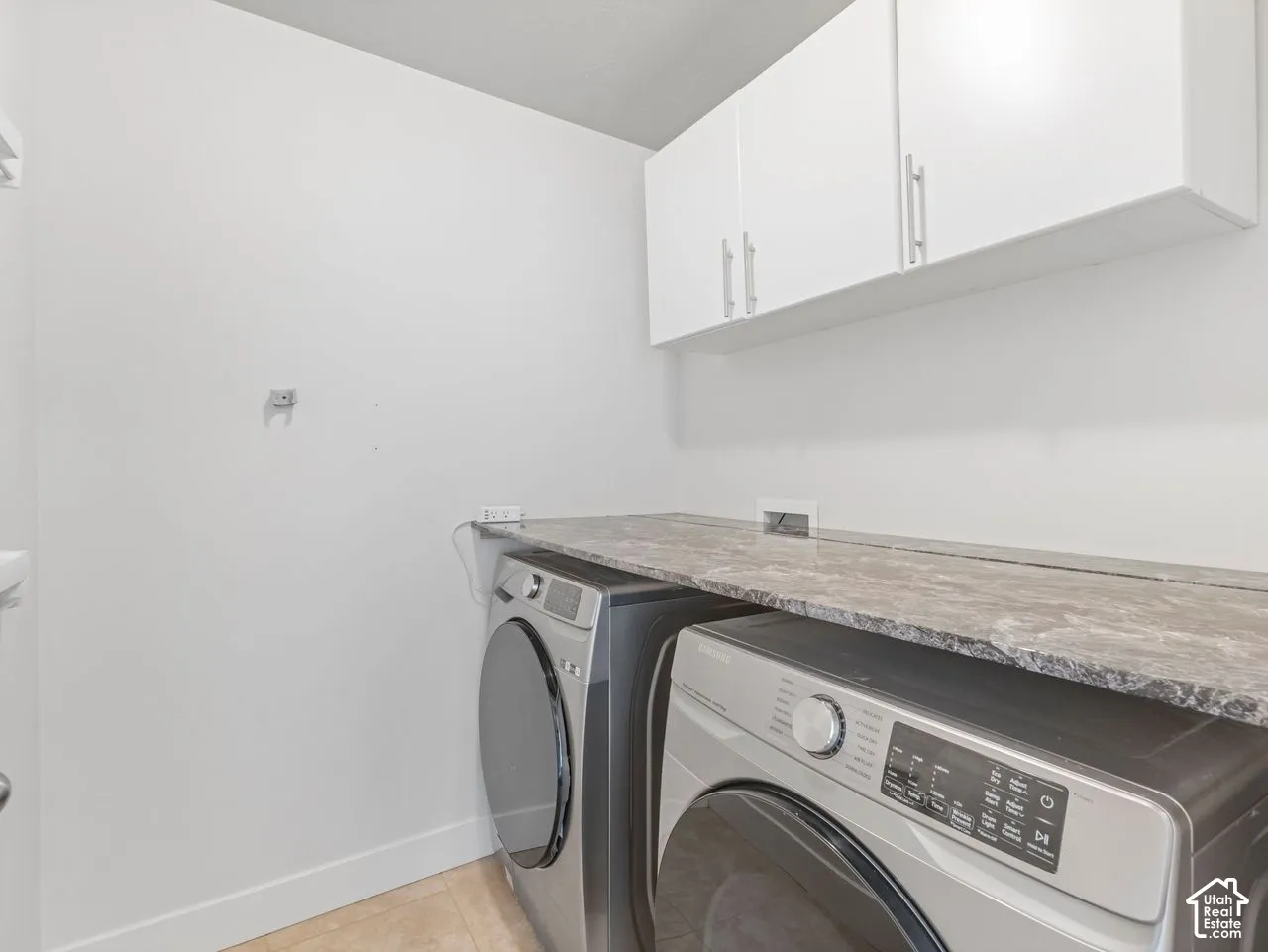 Laundry area featuring white wall-mounted cabinetry, stone-pattern laminate countertop, and tile flooring