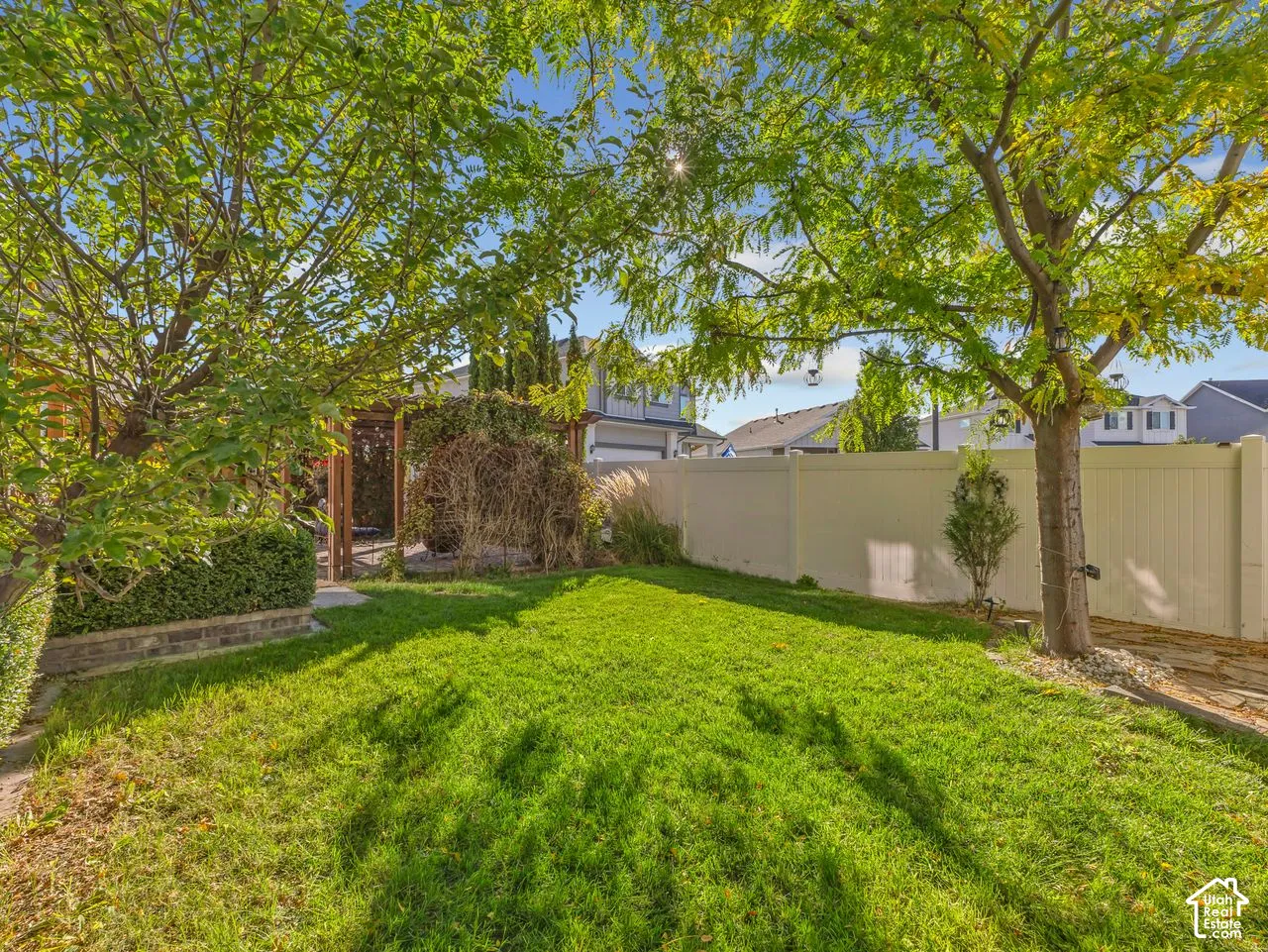 Backyard featuring a manicured lawn, perimeter fencing, mature trees, a wood-frame pergola, and a brick-bordered hedge