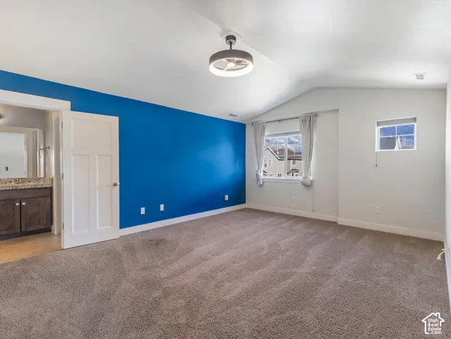 Vaulted ceilings, neutral carpeting, ceiling-mounted light fixture with integrated fan, and painted accent wall