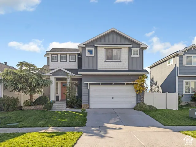 Two-story exterior featuring grey horizontal lap siding, white shingle accents, stone veneer foundation detailing, and an attached two-car garage