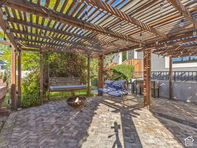 Outdoor living space featuring a wood-beam pergola with integrated string lighting and herringbone-patterned brick paver flooring