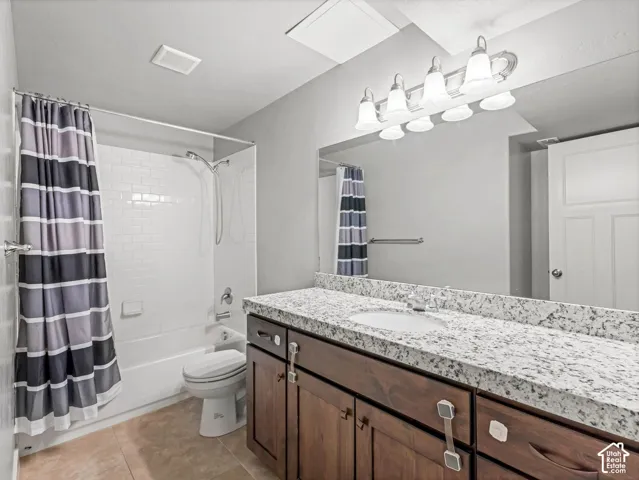Bathroom featuring a vanity with wood-finish cabinetry, speckled stone-composite countertop, full-width mirror, tile flooring, and a tub-shower combination with white subway-style wall tiling