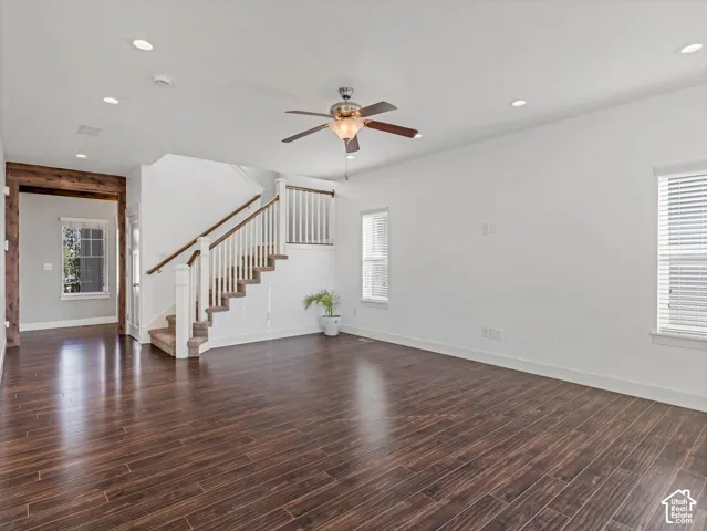 Open-concept interior featuring dark wood-finish flooring, recessed lighting, a ceiling fan with integrated light fixture, and a staircase with white balusters and a dark wood handrail