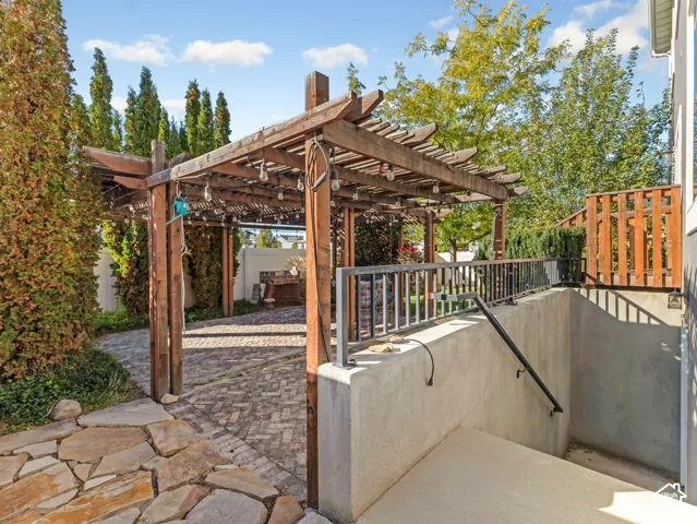 Outdoor living area featuring a wood pergola, herringbone-pattern brick patio, concrete stairway with metal railing, and natural stone hardscaping