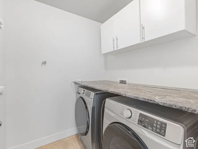 Laundry area featuring white wall-mounted cabinetry, stone-pattern laminate countertop, and tile flooring