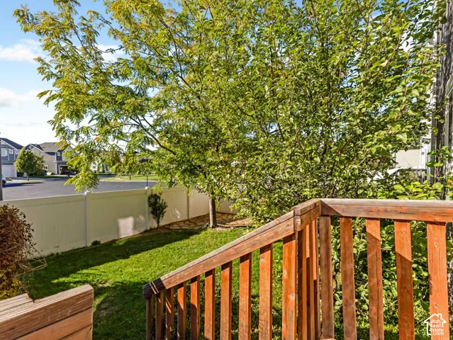Wood-railed deck featuring a grass lawn, white vinyl fencing, and mature trees