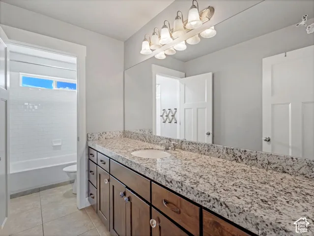 Bathroom vanity featuring stone-finish countertop, undermount sink, multi-drawer cabinetry, large wall-mounted mirror, and multi-bulb fixture