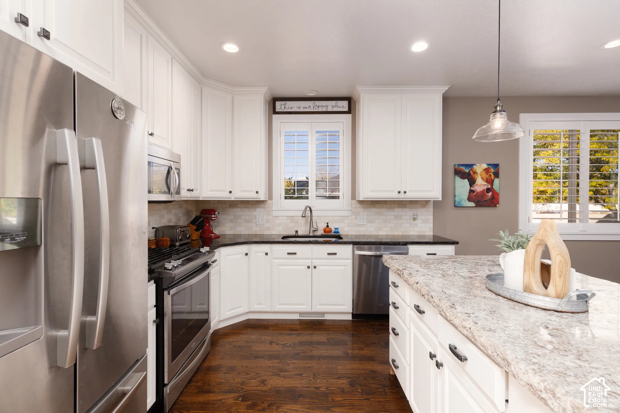Kitchen featuring white cabinetry, stone-surface island countertop, stainless steel appliances, tile backsplash, and wood-finish flooring