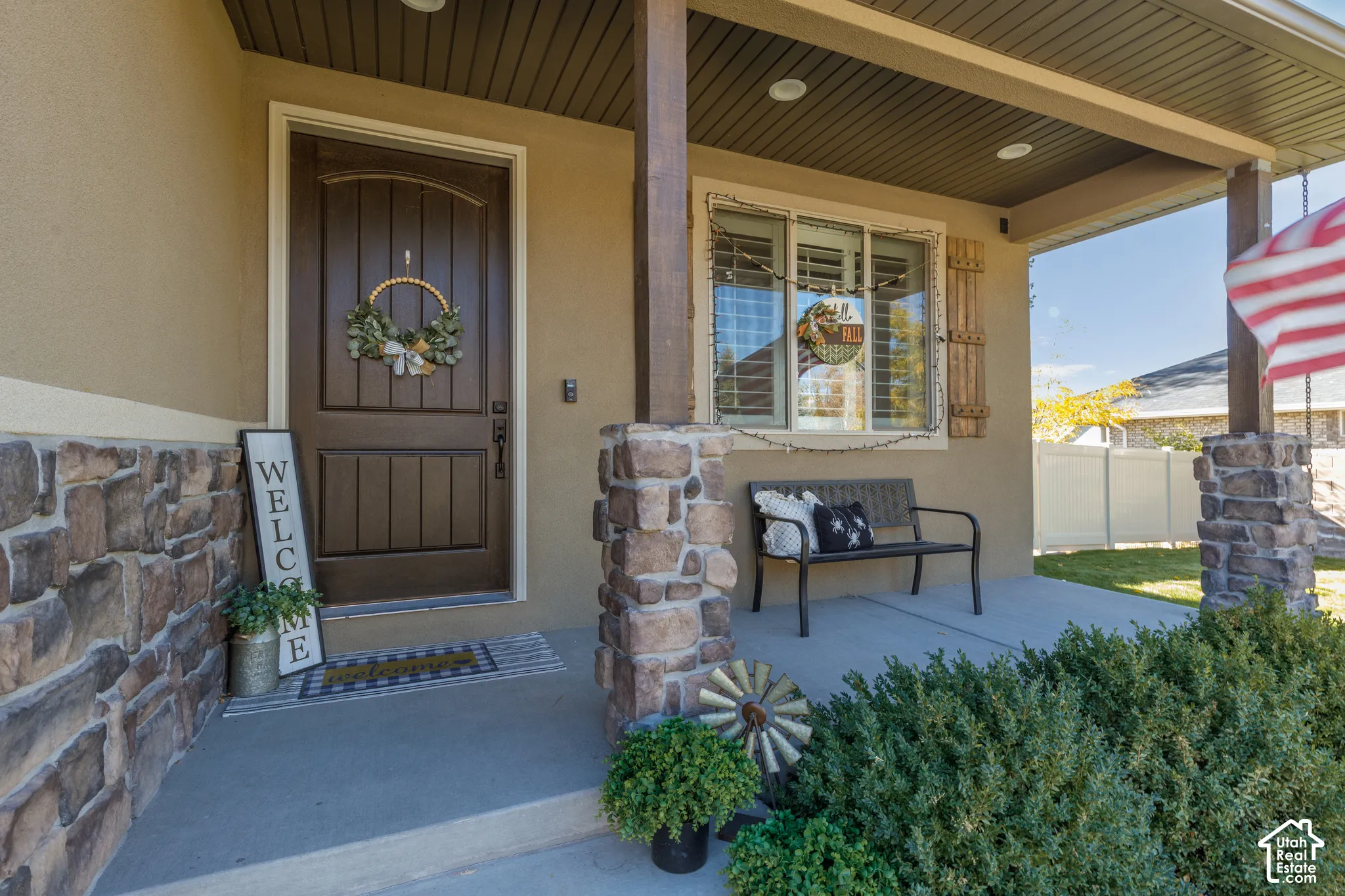Covered entryway featuring a concrete porch, stacked stone exterior accents, dark-stained wood support pillars, and a paneled entry door