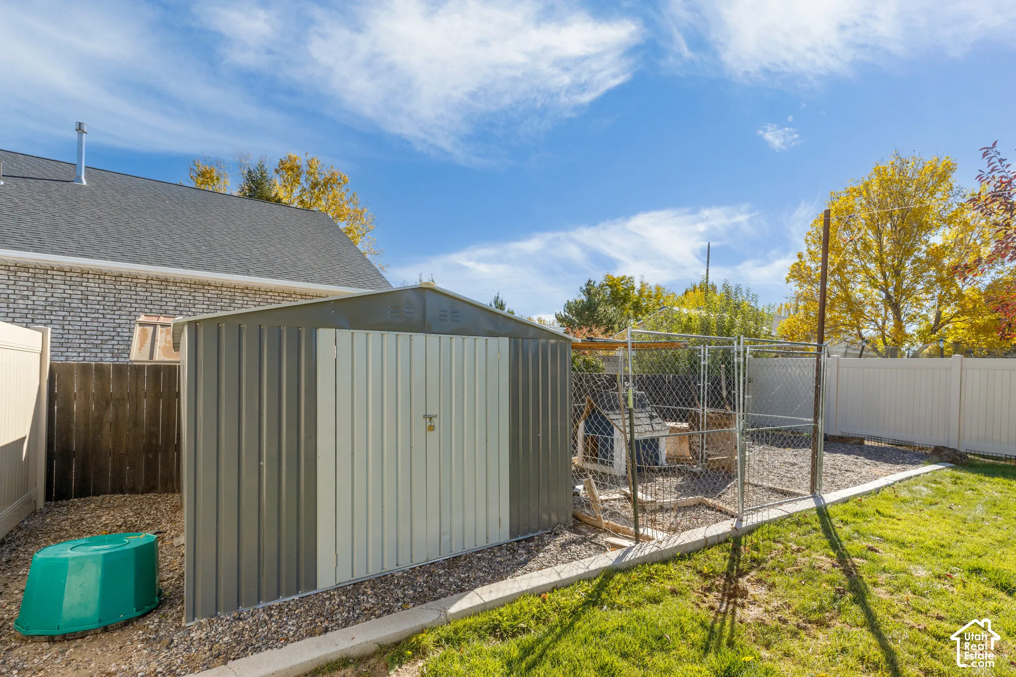 Backyard featuring a metal storage shed, chain-link enclosure, and perimeter vinyl fencing