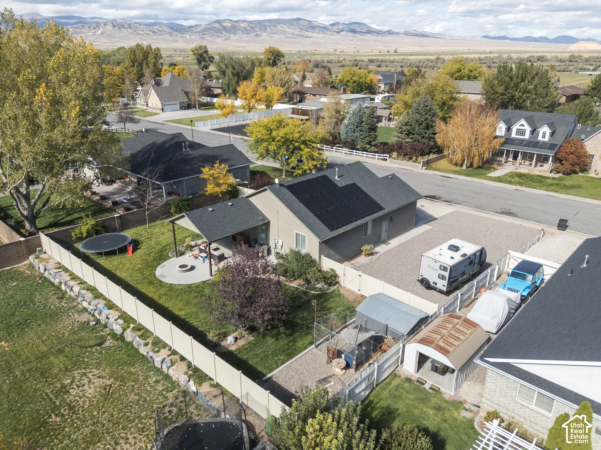 Exterior featuring a dark shingle roof with integrated solar panels, a covered patio area, a concrete fire pit pad, and perimeter vinyl fencing