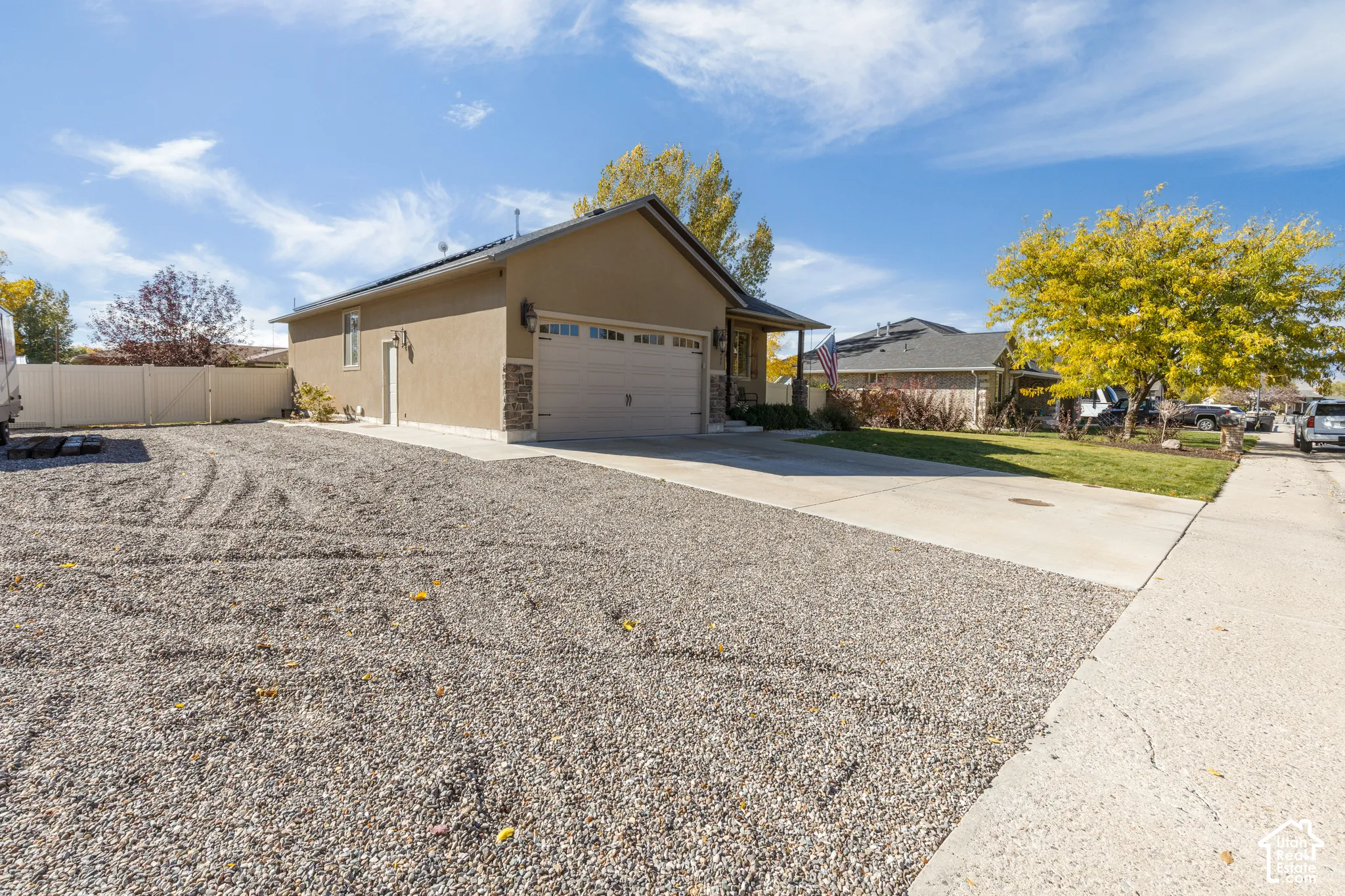 Single-story residence featuring a two-car garage, stone-veneer accents, concrete driveway, and white vinyl perimeter fencing