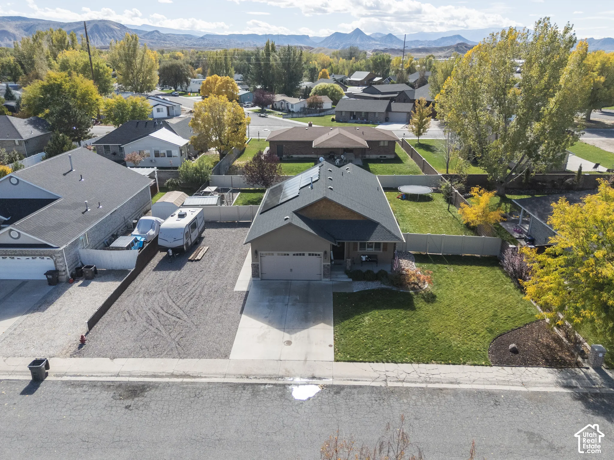 Single-story residence featuring an attached two-car garage, roof-mounted solar panels, an expansive gravel side yard, and a landscaped front lawn with mountain backdrops