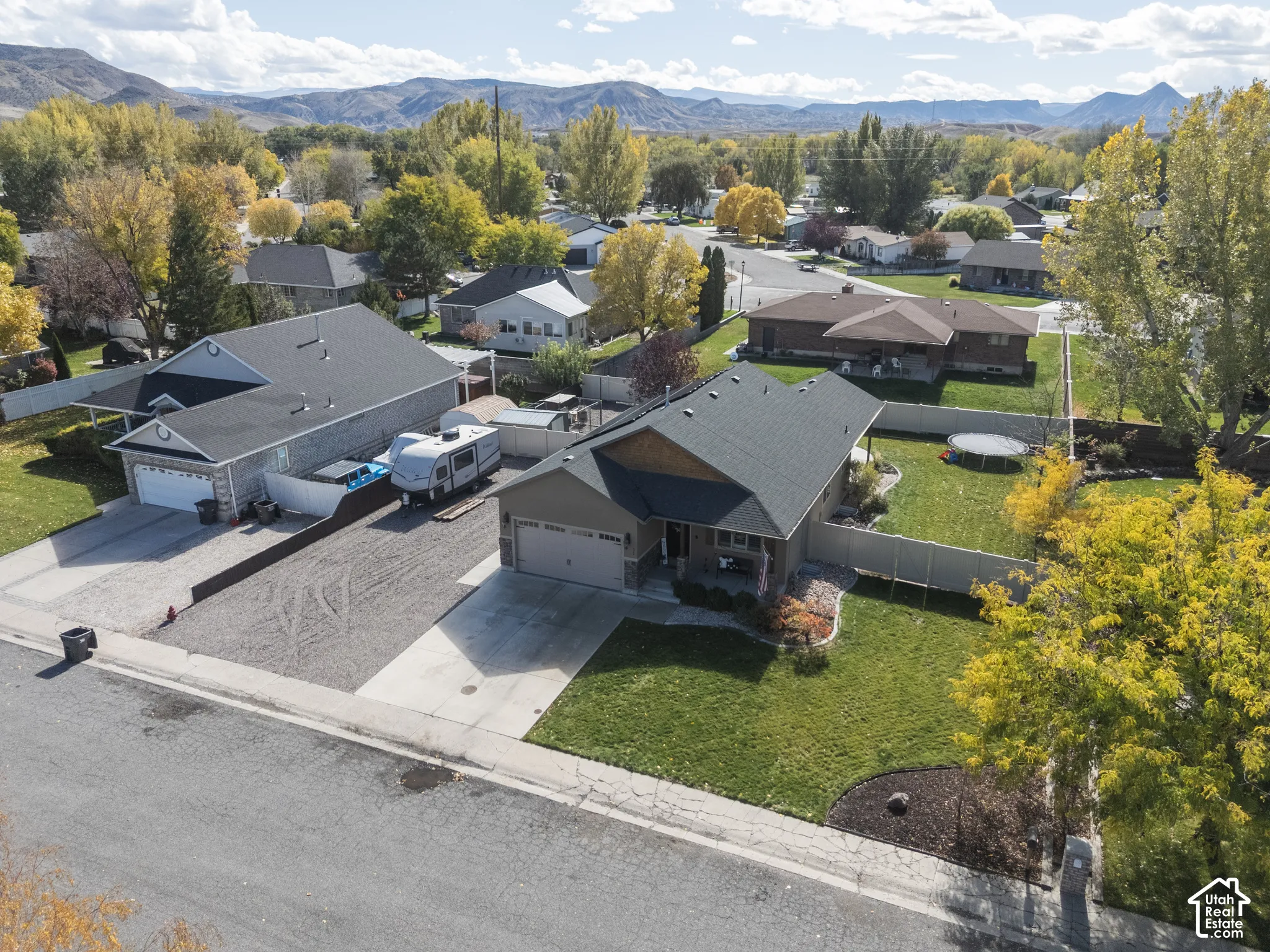 Single-story residence featuring a concrete driveway, attached garage, fenced rear yard, and mature landscaping against a mountain backdrop