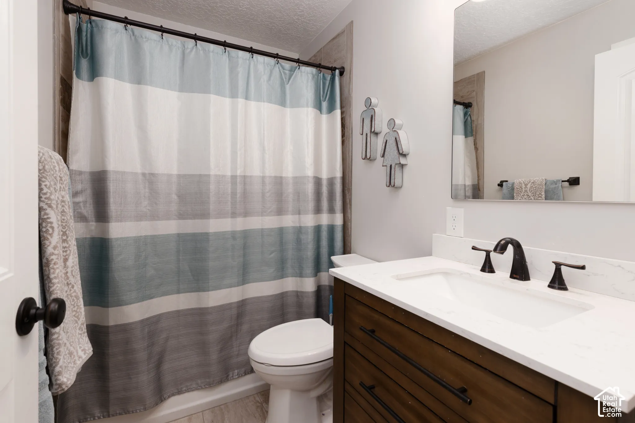 Bathroom featuring a dark wood-finish vanity with a white rectangular sink, quartz countertop, dark metal fixtures, and a frameless mirror