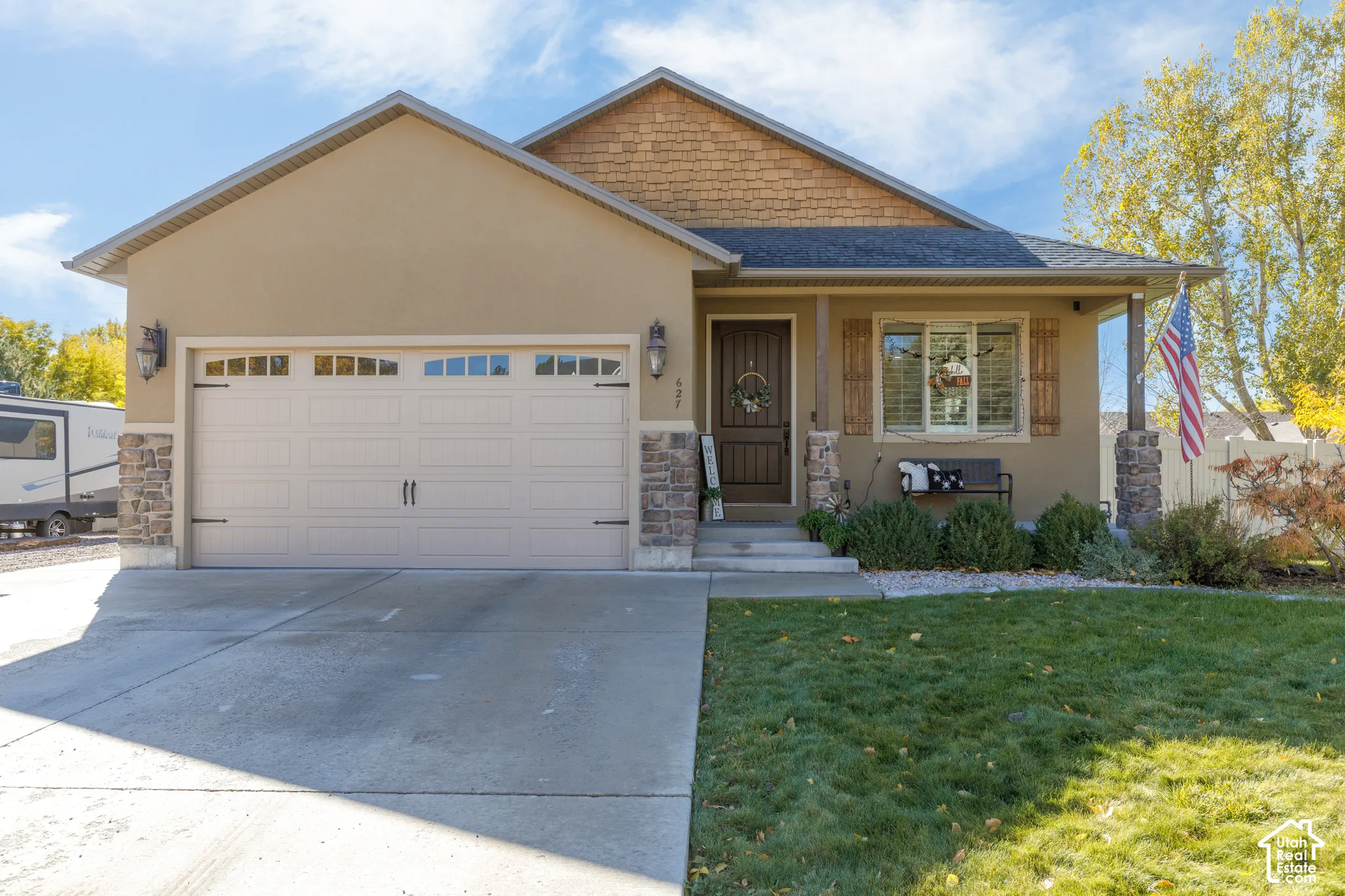 Single-story exterior featuring a stone-accented facade, shake-shingle siding accents, an attached two-car garage, and a covered front porch entry