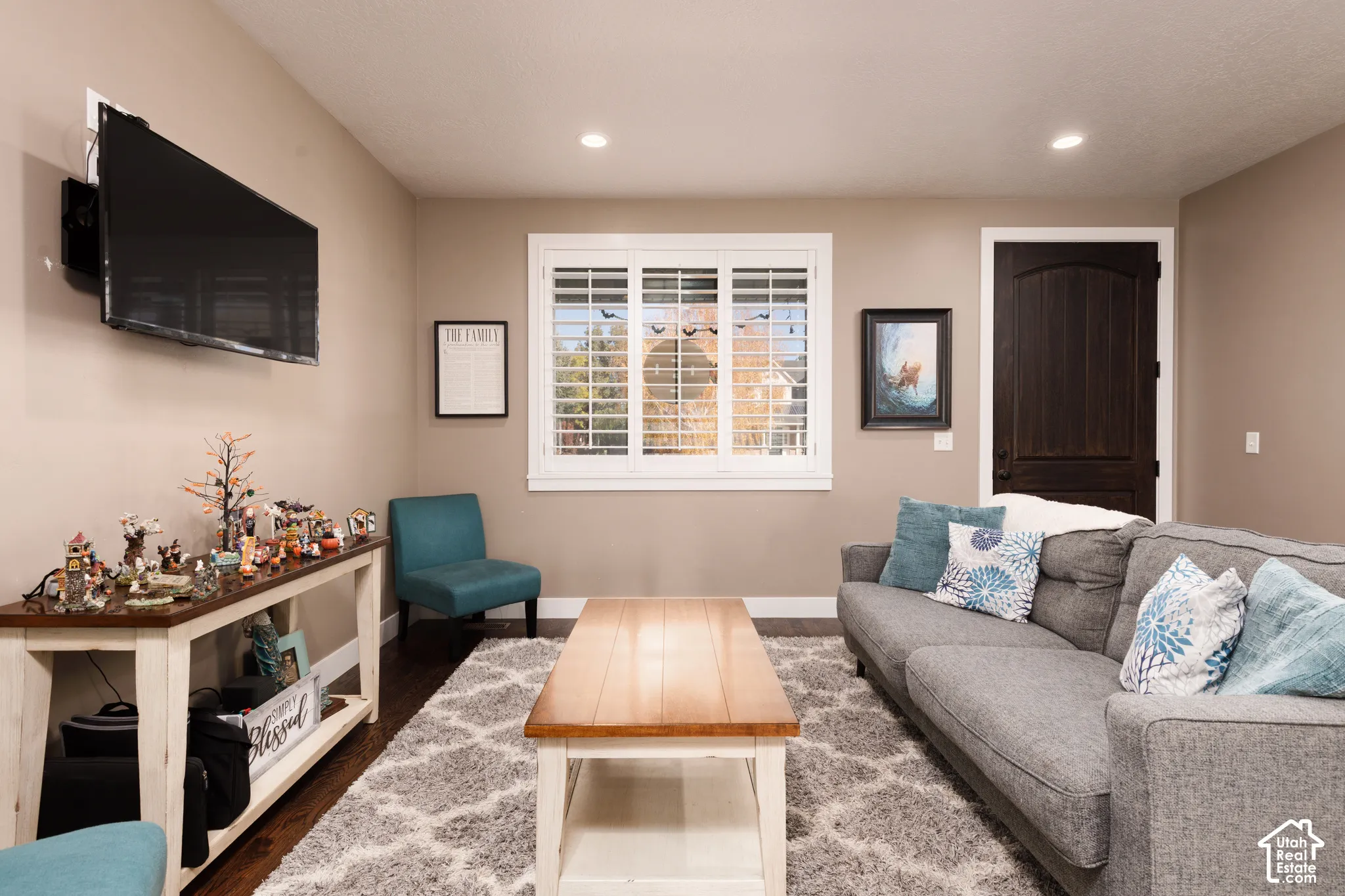 Living area featuring dark wood-finish flooring, recessed lighting, and a window with white louvered shutters