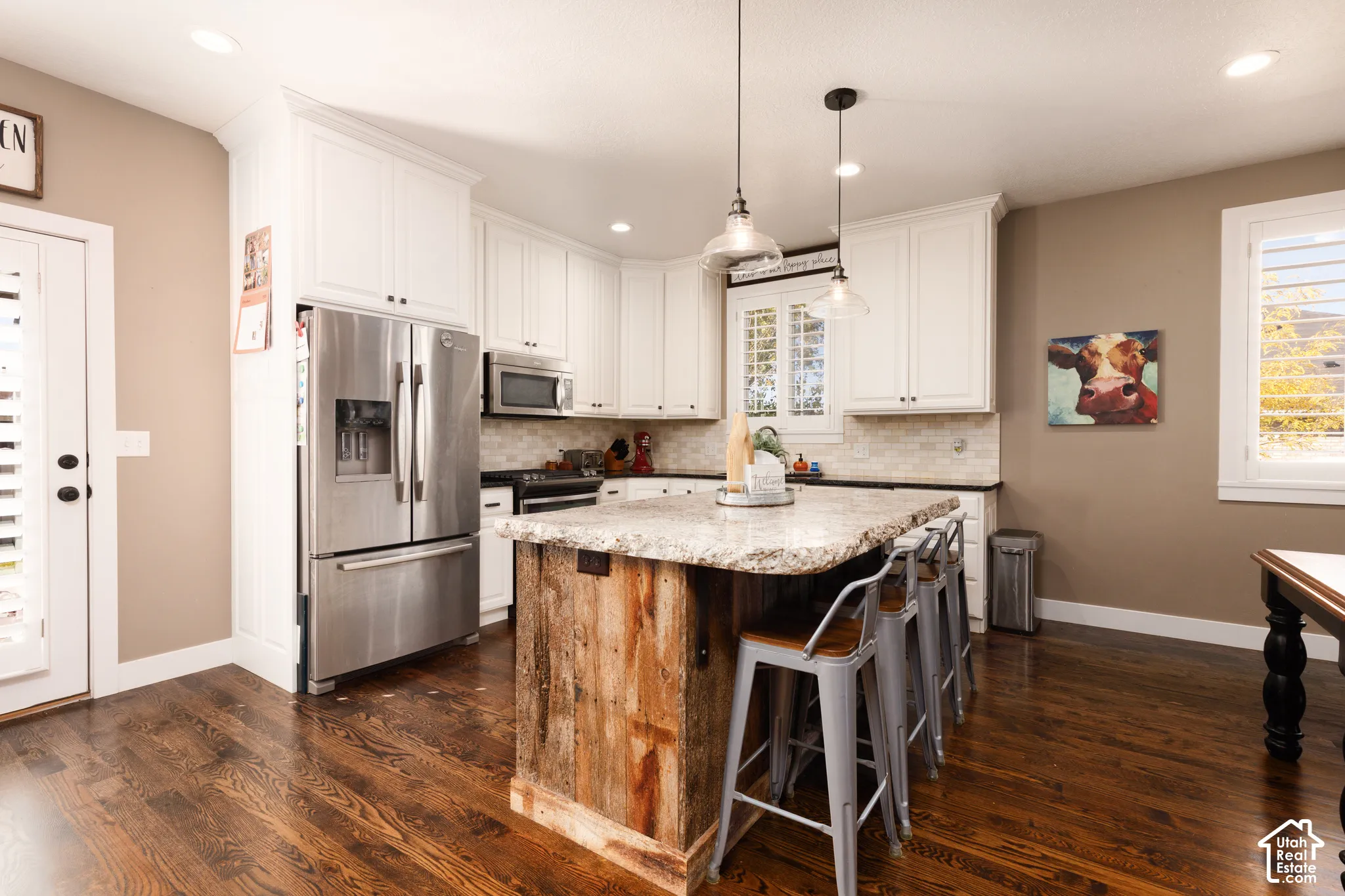 Kitchen featuring white cabinetry, stone-surface island with wood-paneled detailing, stainless steel appliances, tiled backsplash, and wood-finish flooring