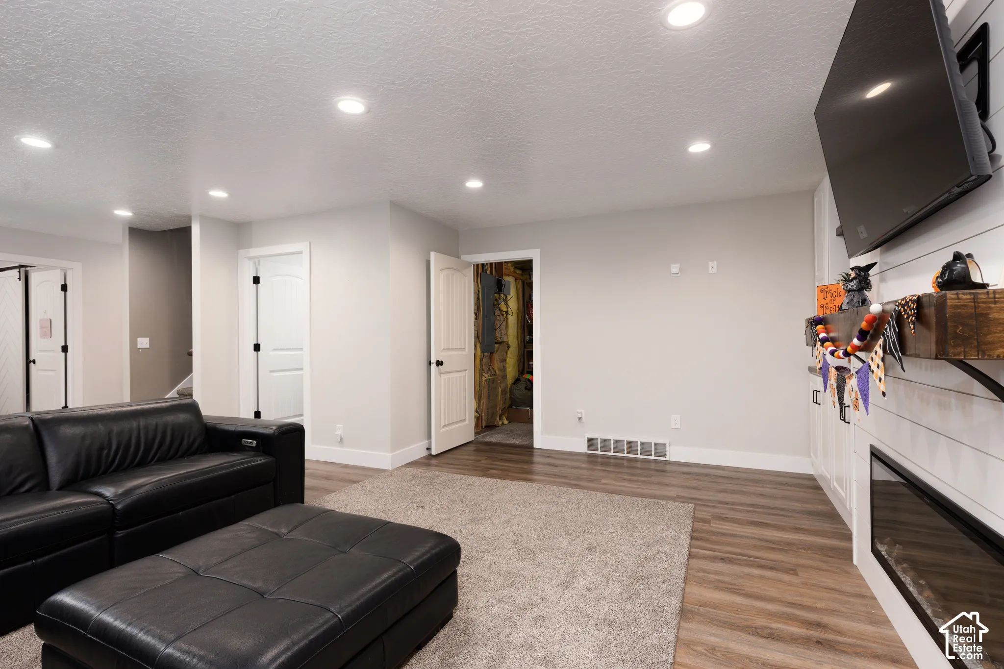 Recessed lighting, wood-finish flooring, built-in horizontal shiplap wall treatment, and electric fireplace with a wood mantel