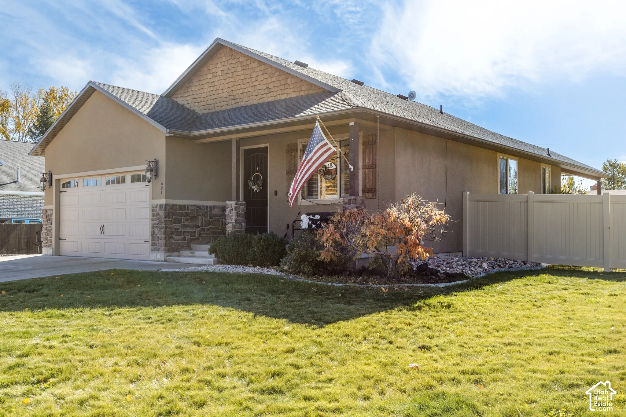 Single-story exterior featuring a stucco and stone facade, attached two-car garage, covered entryway, and privacy vinyl fencing
