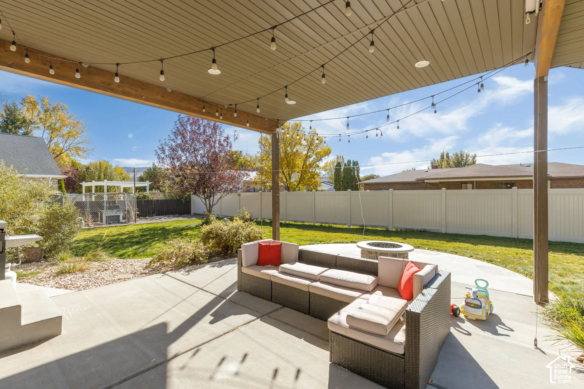 Covered patio featuring a concrete floor, built-in fire pit, string lighting, and a vinyl privacy fence enclosing the backyard