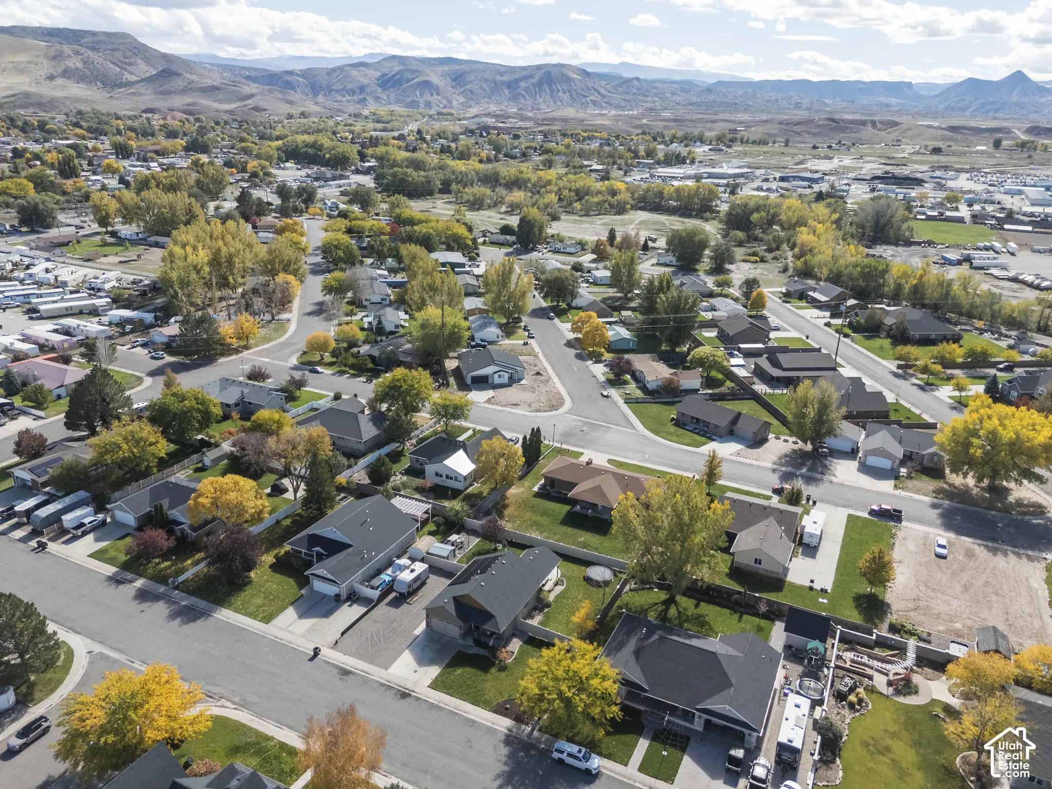 Aerial perspective of a suburban neighborhood featuring mature trees, paved streets, residential lots, and a distant mountain range backdrop
