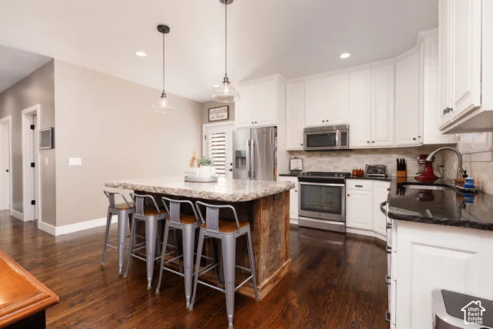 Kitchen featuring white cabinetry, stone countertops, wood-finish flooring, a central island with a wood base, and stainless steel appliances