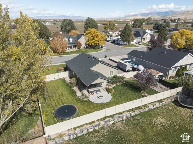 Fenced backyard featuring a covered patio, hardscape fire pit area, expansive lawn, and mountain scenery