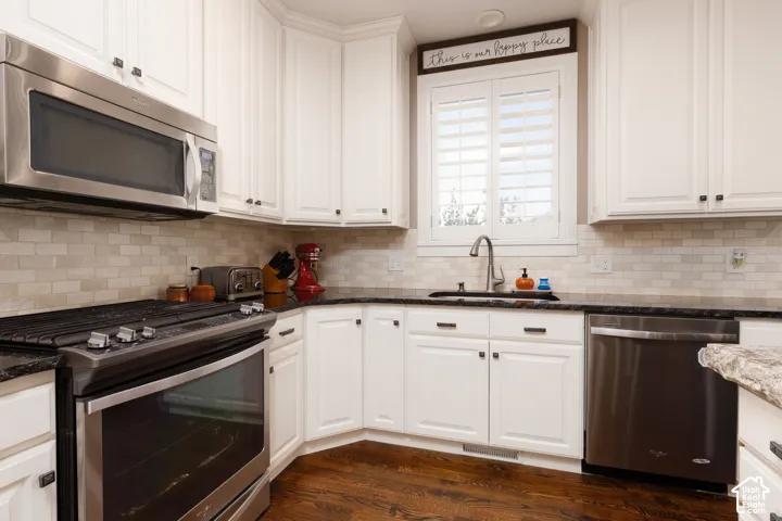 Kitchen featuring white shaker-style cabinetry, dark stone countertops, stainless steel appliances, a subway-style tiled backsplash, and wood-finish flooring
