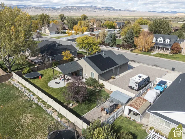 Exterior featuring a dark shingle roof with integrated solar panels, a covered patio area, a concrete fire pit pad, and perimeter vinyl fencing