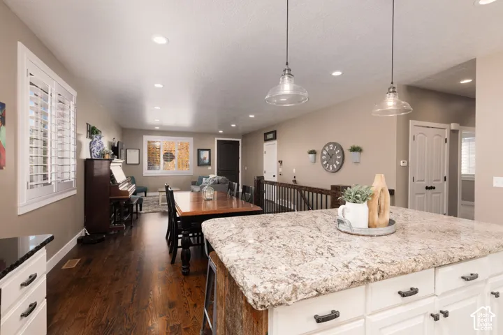 Open-concept area featuring white shaker-style cabinetry, patterned stone countertops, wood-finish flooring, recessed lighting, and glass pendant light fixtures