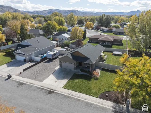Single-story residence featuring a concrete driveway, attached garage, fenced rear yard, and mature landscaping against a mountain backdrop